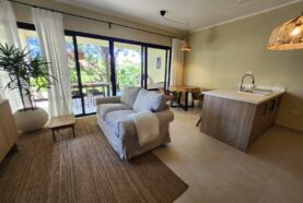 Modern Mediterranean-style white apartment building with terracotta roof tiles, palm trees, balconies, and landscaped garden in Pro Cab, Cabarete