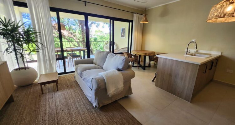 Modern Mediterranean-style white apartment building with terracotta roof tiles, palm trees, balconies, and landscaped garden in Pro Cab, Cabarete